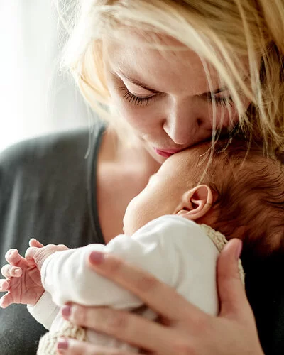 Eine Mutter hält ihr Neugeborenes zärtlich im Arm, Körperkontakt stärkt die Eltern-Kind-Bindung.