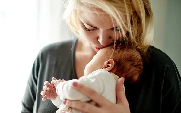 Eine Mutter hält ihr Neugeborenes zärtlich im Arm, Körperkontakt stärkt die Eltern-Kind-Bindung.