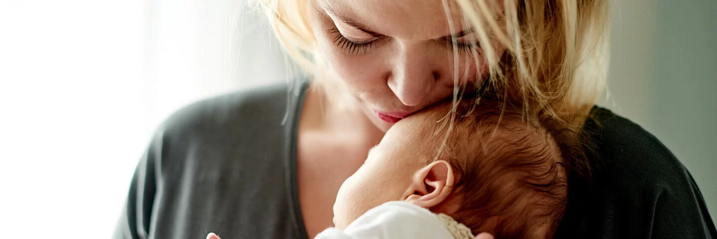 Eine Mutter hält ihr Neugeborenes zärtlich im Arm, Körperkontakt stärkt die Eltern-Kind-Bindung.