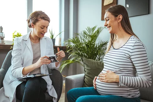 Junge Frau lächelt, während sie zusammen mit ihrer Hebamme das Ultraschallbild ihres Babys betrachtet.