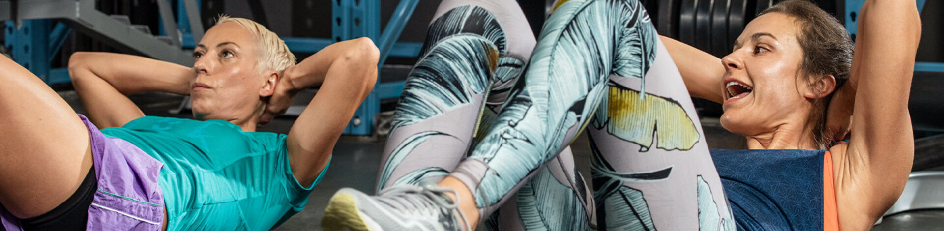 Das Bild zeigt zwei Frauen in Sportkleidung in einem Fitnessstudio, die Sit-ups machen.