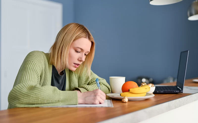 Eine Frau mit Reizdarmsyndrom schreibt ein Symptom- und Ernährungstagebuch, um Auslöser für die Beschwerden zu identifizieren.