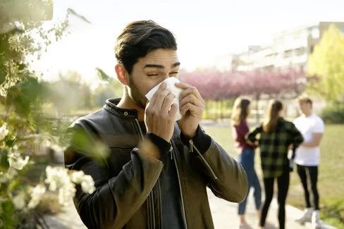 Ein junger Mann ist im Freien und putzt seine Nase. Was gegen eine Pollenallergie hilft, verrät der Beitrag. 
