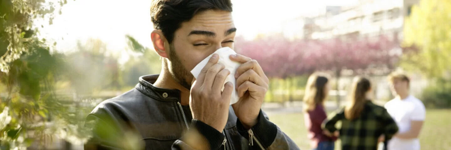 Ein junger Mann ist im Freien und putzt seine Nase. Was gegen eine Pollenallergie hilft, verrät der Beitrag. 