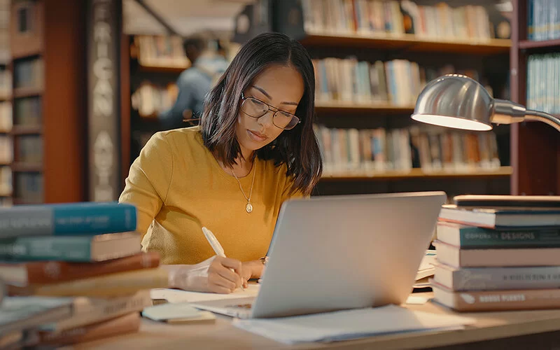 Eine junge Frau sitzt in der Bibliothek am Laptop und schreibt.