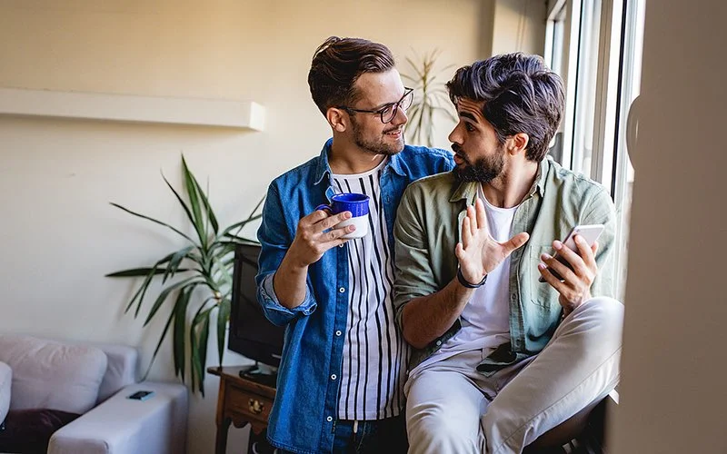 Ein männliches Paar führt ein angeregtes Gespräch im Wohnzimmer.