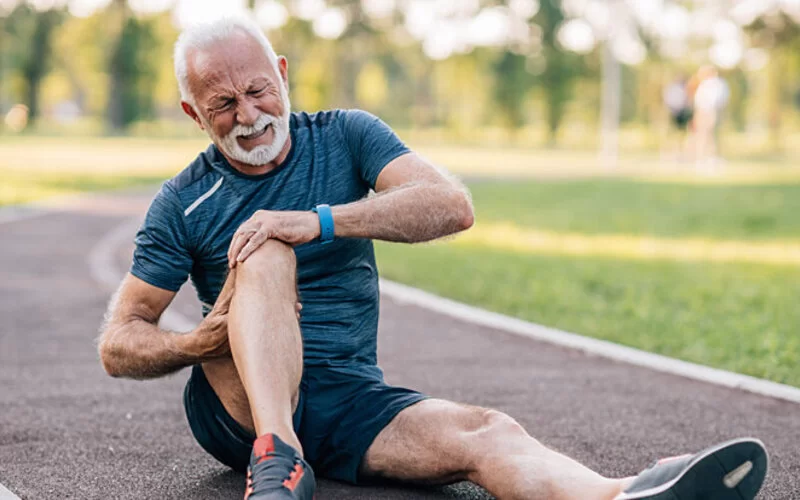 Ein älterer Mann sitzt auf einer Laufstrecke und fasst sich ans schmerzende Knie, das von einer Tendopathie betroffen ist.