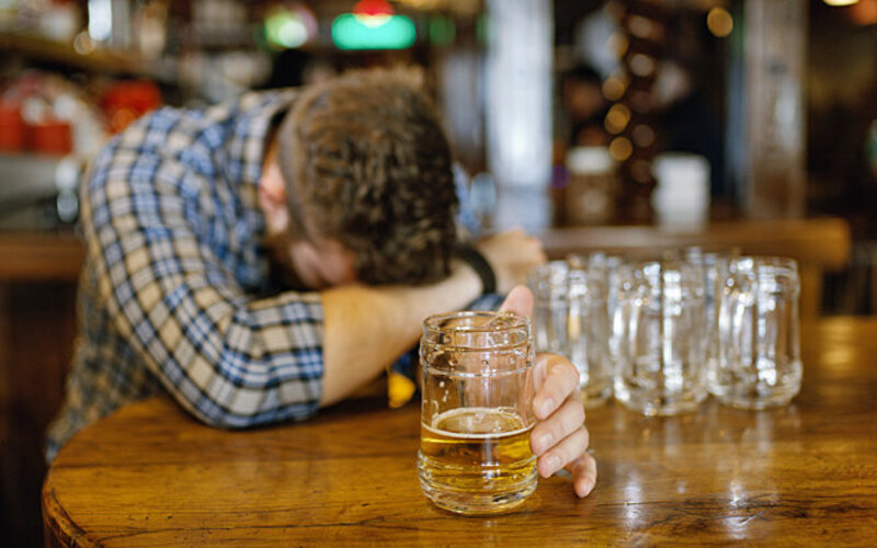 Ein Mann liegt mit dem Kopf auf dem Tisch und hält ein Bierglas in der Hand.