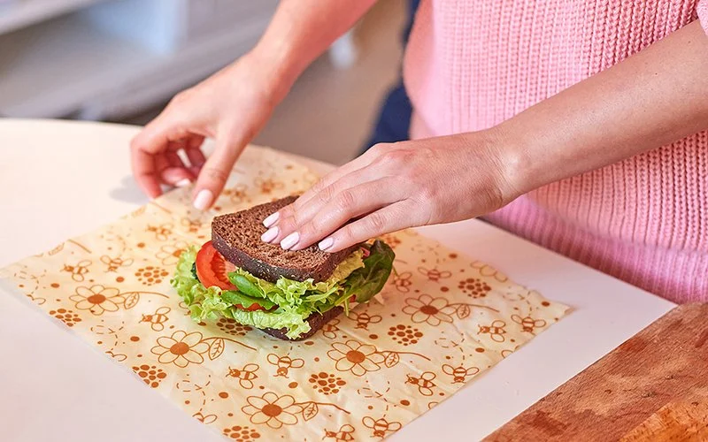 Nahaufnahme von zwei Händen einer Person, die ein belegtes Brot in ein Bienenwachstuch einpacken.