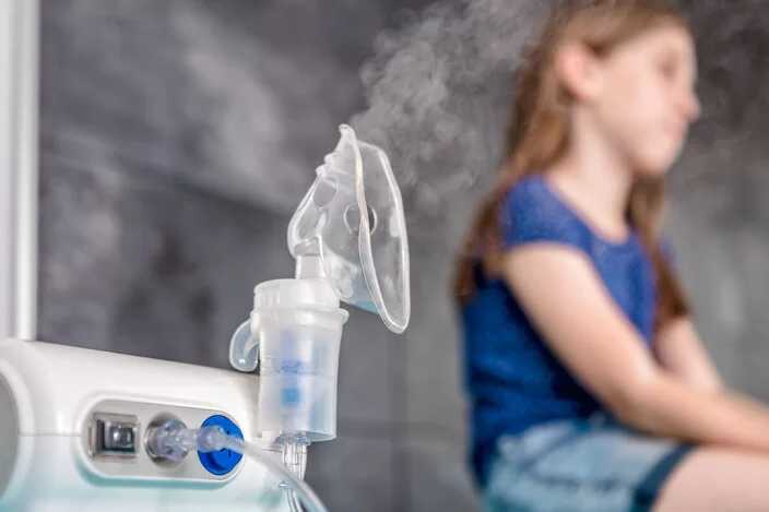 Ein Mädchen sitzt neben einem Inhalationsgerät.