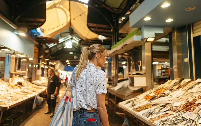 Eine junge Frau geht über einen Fischmarkt und schaut sich die ausgelegte Ware an.