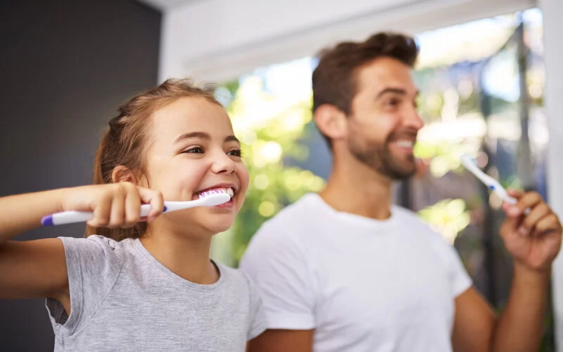 Vater und Tochter putzen sich die Zähne für ein gesundes Zahnfleisch.