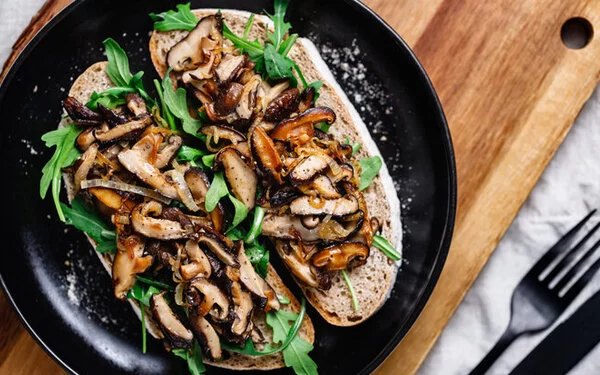 Vegetarisches Pilzgericht mit leckerem Sauerteigbrot und Rucola auf einem schwarzen Teller