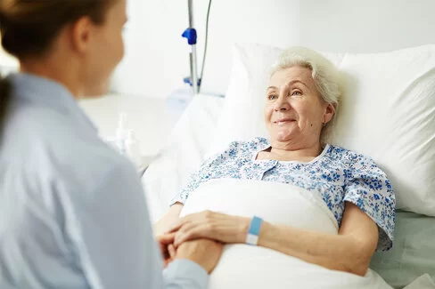 Eine ältere Frau liegt in einem Krankenhausbett und hält die Hand von einer jüngeren Frau.