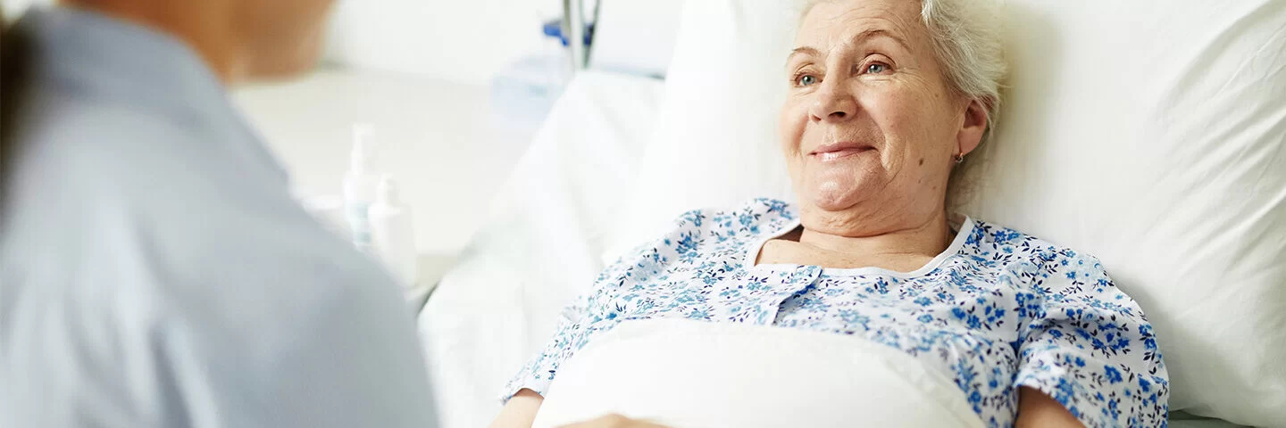Eine ältere Frau liegt in einem Krankenhausbett und hält die Hand von einer jüngeren Frau. 