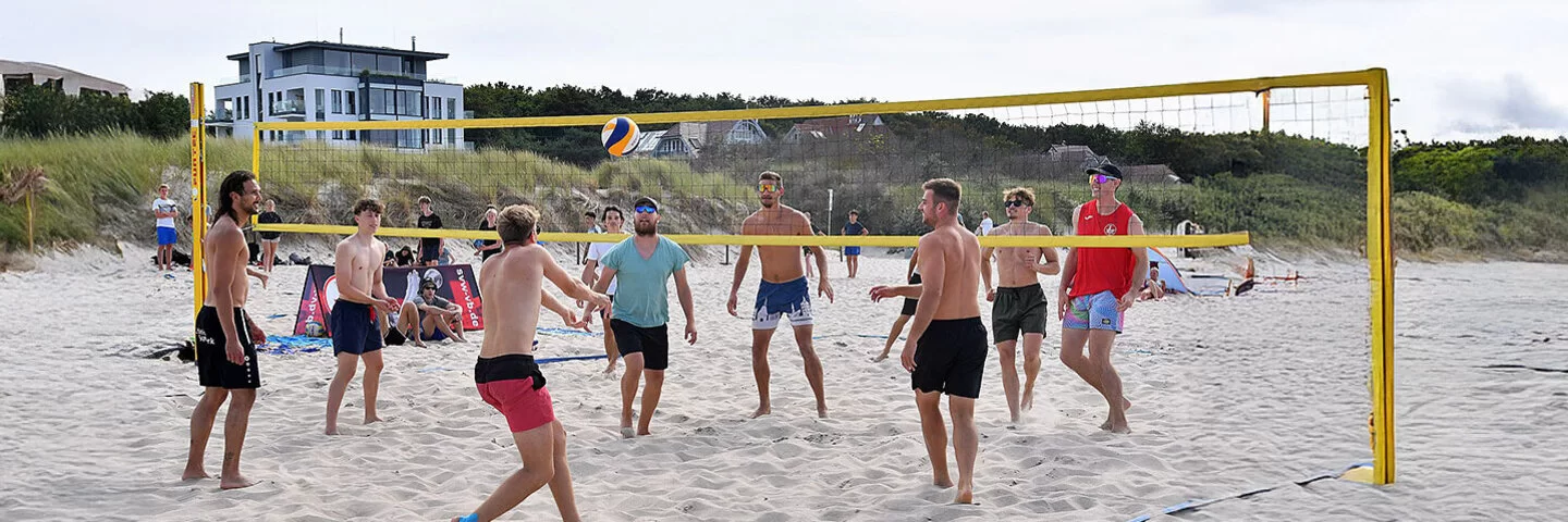 Eine Gruppe junger Männer spielt am Strand ein Beachvolleyball-Turnier.