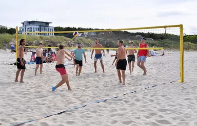 Eine Gruppe junger Männer spielt am Strand ein Beachvolleyball-Turnier.