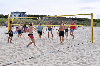 Eine Gruppe junger Männer spielt am Strand ein Beachvolleyball-Turnier.