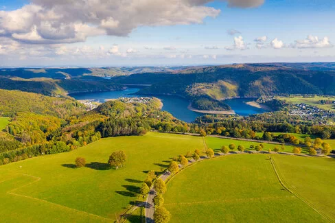 Das Bild zeigt Wälder und Wiesen aus erhöhter Perspektive, in der Entfernung ist der Eifeler Rursee zu erkennen.