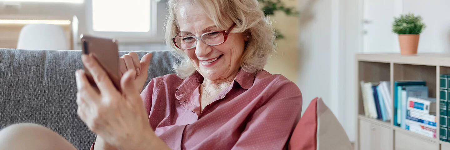 Eine ältere Frau sitzt mit dem Smartphone auf dem Sofa – und zeigt so, dass Digitalisierung auch im Alter möglich ist.