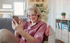 Eine ältere Frau sitzt mit dem Smartphone auf dem Sofa – und zeigt so, dass Digitalisierung auch im Alter möglich ist.