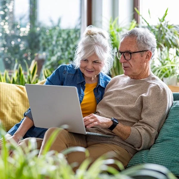 Ein Seniorenpaar sitzt mit einem Laptop auf der Wohnzimmercouch.