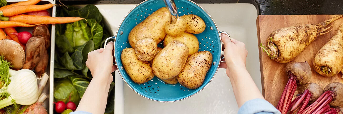 Eine Frau wäscht in einem Sieb Kartoffeln ab.