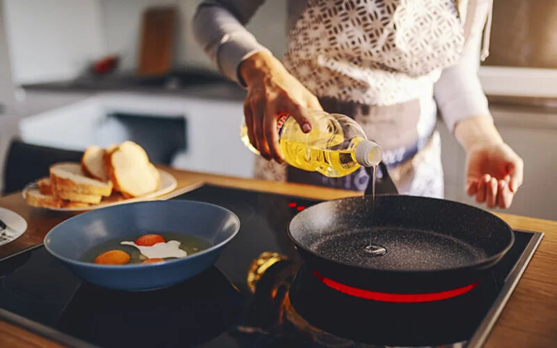 Eine Frau gießt Öl zum Braten in die Pfanne.