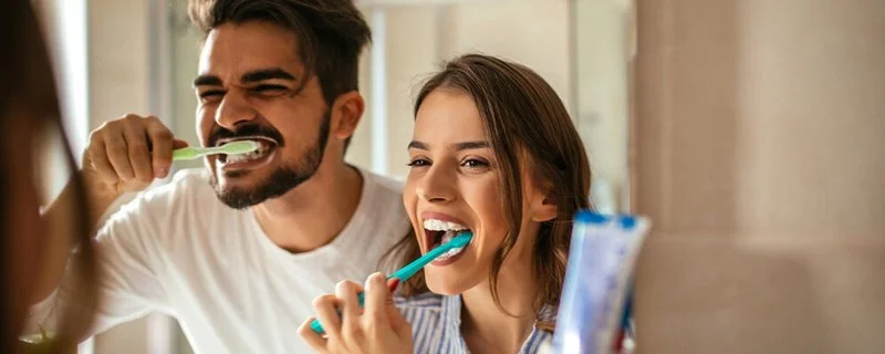 Ein Paar putzt zusammen vor dem Badezimmerspiegel die Zähne.