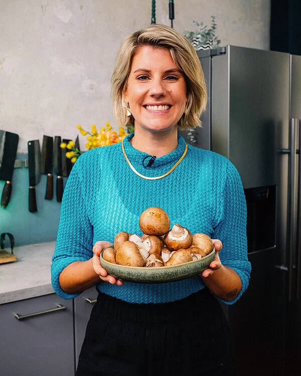Das Bild zeigt die Fernsehköchin Felicitas Then, die mit lächelndem Gesichtsausdruck eine Schüssel mit braunen Champignons in der Hand hält.