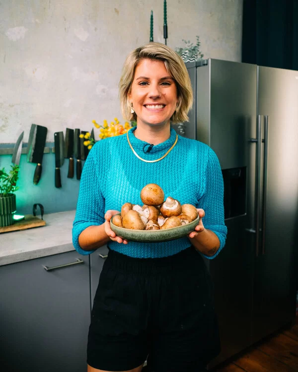 Das Bild zeigt die Fernsehköchin Felicitas Then, die mit lächelndem Gesichtsausdruck eine Schüssel mit braunen Champignons in der Hand hält.