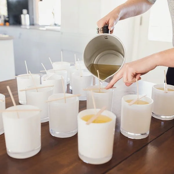 Eine Frau macht Kerzen selber – sie gießt flüssiges Wachs in Gläser mit Dochten.