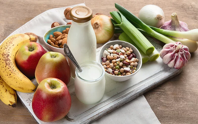 Auf einem Küchenbrett sind probiotische Lebensmittel wie Milch und Joghurt sowie weitere gesunde Gemüse- und Obstsorten für den Darm drapiert.