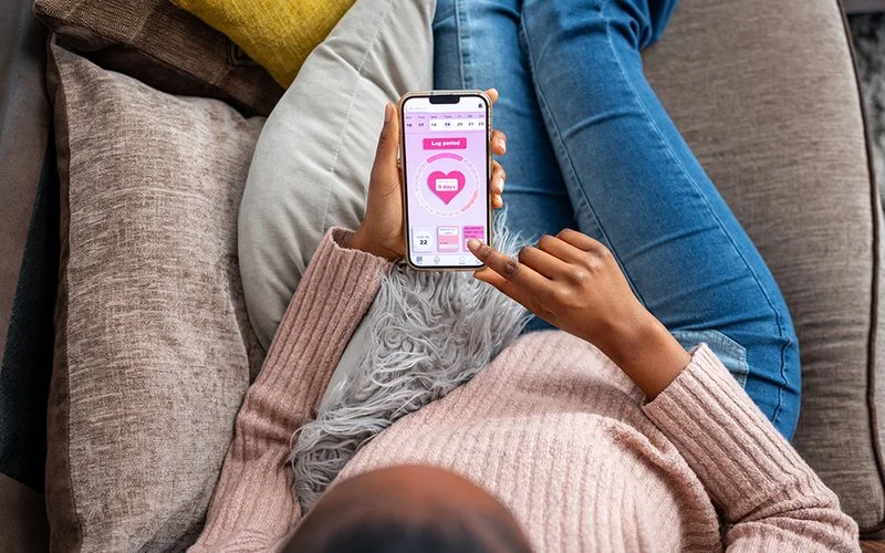 Eine Frau checkt ihren Zyklus in einer Zyklus-App auf dem Smartphone.