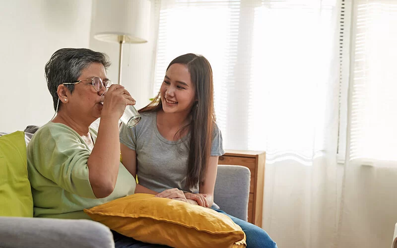 Jugendliche reicht ihrer pflegebedürftigen Mutter ein Glas Wasser, sie gehört zu den Young Carers.