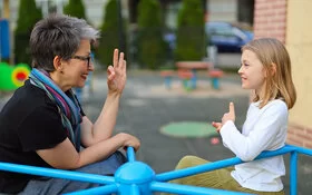 Mutter und Tochter sind auf einem Spielplatz und sitzen in einem kleinen Karussell, sie unterhalten sich in Gebärdensprache miteinander.