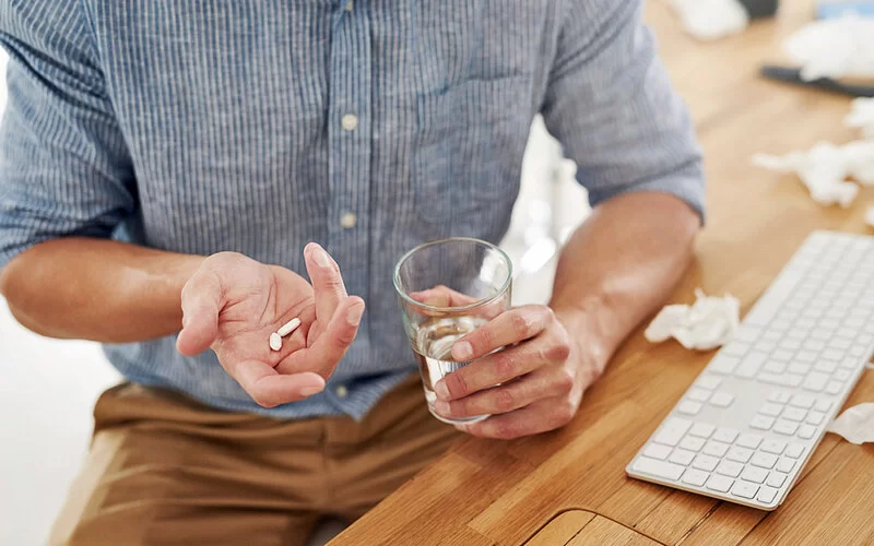Ein Mann hält eine Tablette und ein Glas Wasser in der Hand und überlegt, ob er eine Schmerztablette nehmen soll.