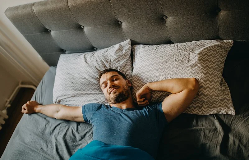 Ein Mann streckt sich lächelnd im Bett.
