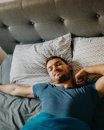 Ein Mann streckt sich lächelnd im Bett.