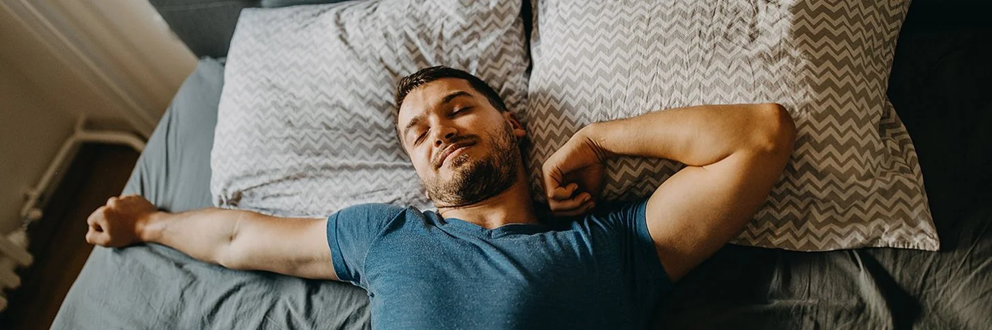 Ein Mann streckt sich lächelnd im Bett.