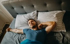 Ein Mann streckt sich lächelnd im Bett.