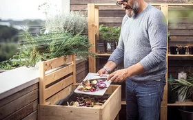 Ein Mann gibt Essensreste in den Kompost auf dem Balkon.