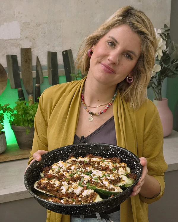 Felicitas Then hält eine emaillierte Auflaufform mit gefüllten Zucchini in die Kamera.