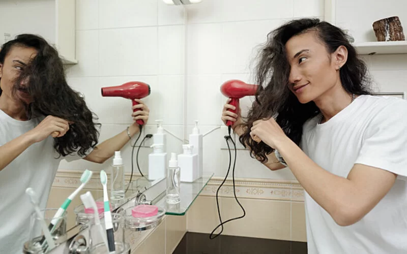 Junger Mann fönt sich seine langen Haare.