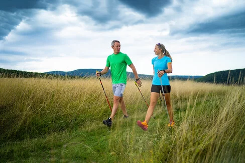 Ein Mann und eine Frau walken mit Stöckern über einen Feldweg.