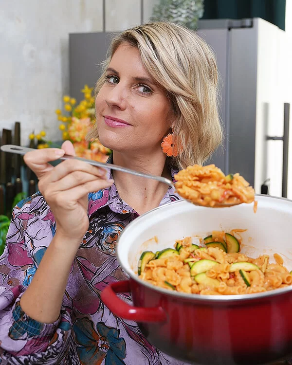 TV-Köchin Felicitas Then hält einen Topf mit Pasta, Zucchini und Kichererbsen in ihren Händen und präsentiert die One-Pot-Pasta freundlich lachend in die Kamera.