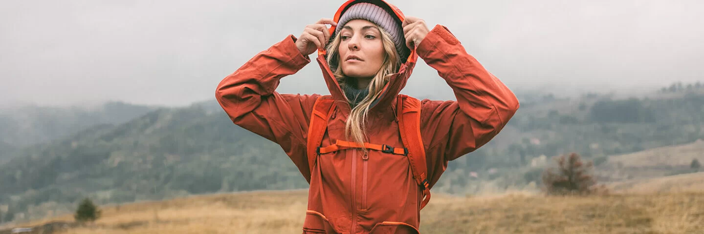 Junge Frau zieht sich die Kapuze ihrer Regenjacke über den Kopf.