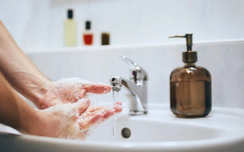 Eine Person wäscht sich mit Seife die Hände über dem Waschbecken.