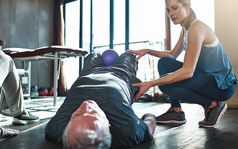 Eine Physiotherapeutin unterstützt einen Mann beim Beckenbodentraining.