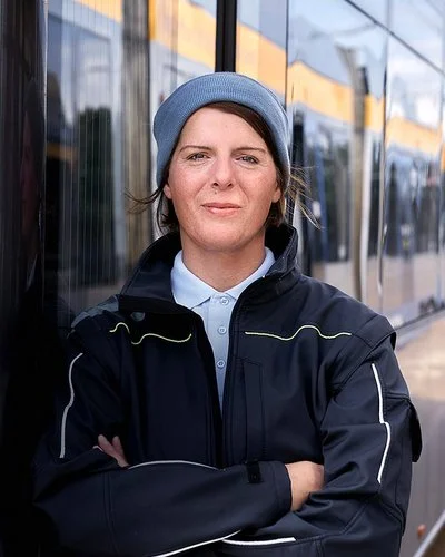 Die Busfahrerin Angela Rossberg steht mit vor dem Oberkörper verschränkten Armen vor einem Bus und schaut selbstbewusst in die Kamera.